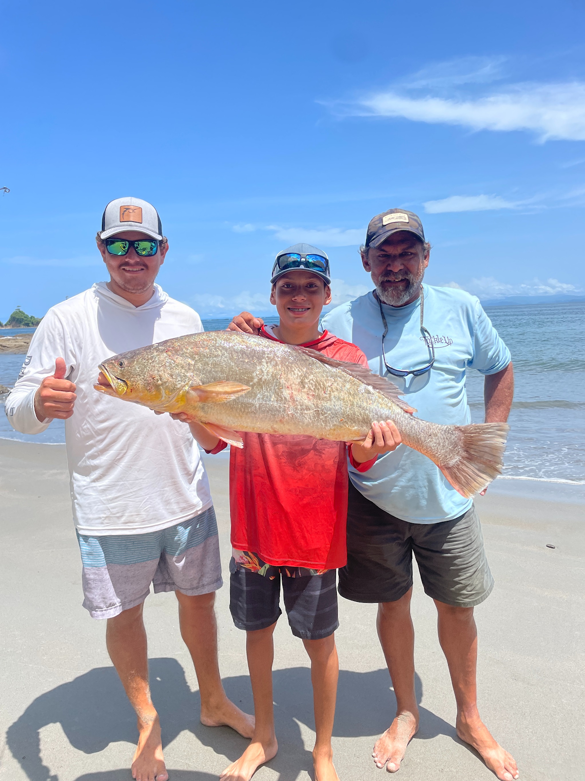 Three people on a beach with a large fish