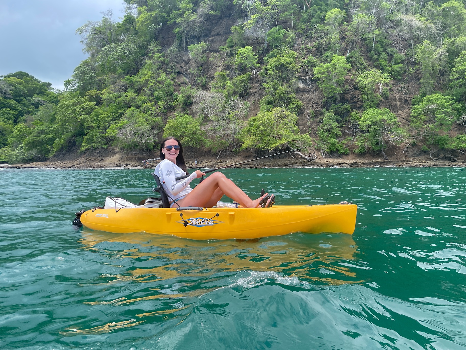 Angler in a yellow kayak fishing near a lush tropical coastline